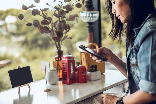 De vrouwenzitting van Azië in de koffiewinkel en het gebruiken van mobiele telefoon