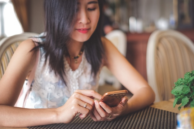 De vrouwenzitting van Azië in koffiewinkel en het gebruiken van mobiele telefoon voor het controleren van sociale media