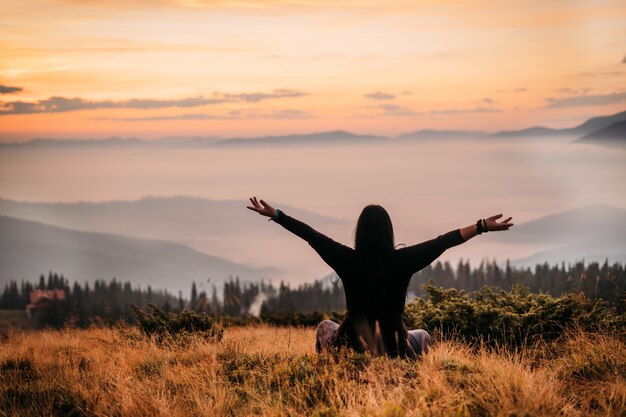 De vrouwenzitting van de yoga bovenop een berg bij zonsopgang.