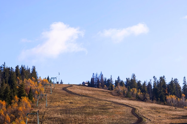 De weg die leidt naar de top van de berg Natuurlijke achtergrond van herfst bergen met gele bomen en sparren met wolken in de blauwe lucht