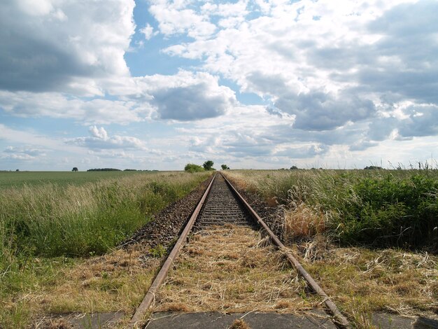 Foto de weg loopt door een veld tegen een bewolkte lucht.