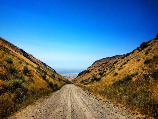 Foto de weg tussen de bergen tegen een heldere blauwe hemel.