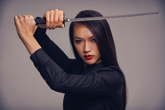 De weg van de ninja Studioportret van een mooie jonge vrouw in een vechtsportoutfit die een samoeraizwaard hanteert