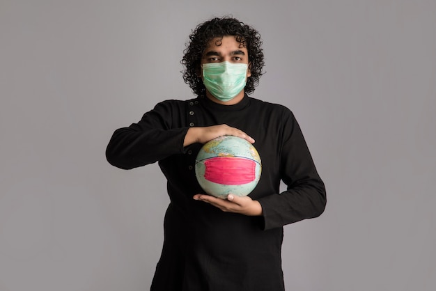 De wereldbol van de jonge mensenholding met een geneeskunde gezichtsmasker. Wereldepidemie van coronavirus concept.