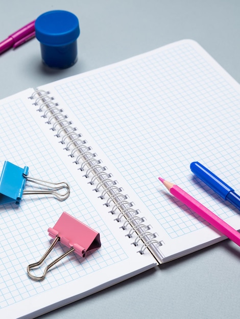 De werkplek van een schoolkind met een opengeslagen notitieboekje, potloden, pennen, penselen, aquarellen en ander briefpapier op een lichttafel