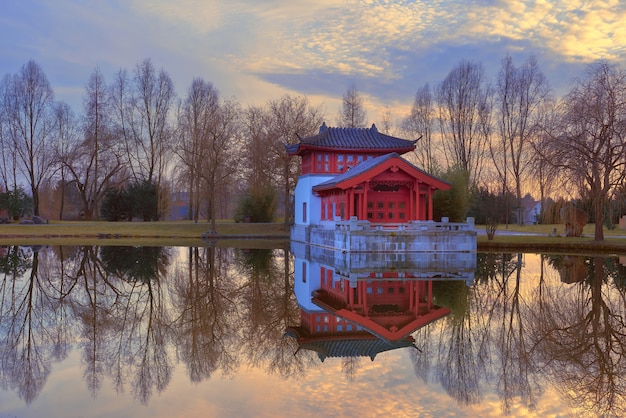 De wintermening van formele Chinese tuin met decoratieve pavillion op een zonsondergang