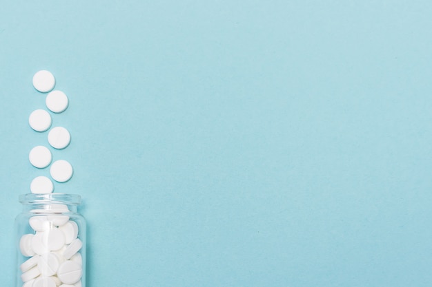 Foto de witte medische tabletten in glasfles op blauw, sluiten omhoog.