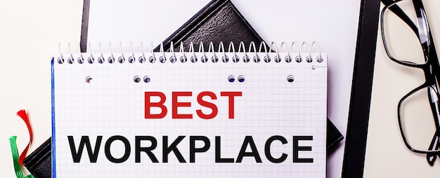 De woorden BEST WORKPLACE zijn in het rood geschreven in een wit notitieboekje naast een bril met een zwart montuur