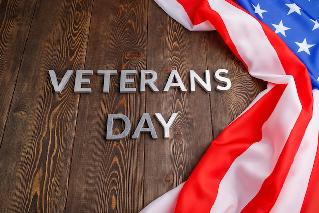 De woorden Veteranendag gelegd met zilveren metalen letters op een houten bord met verfrommelde Amerikaanse vlag