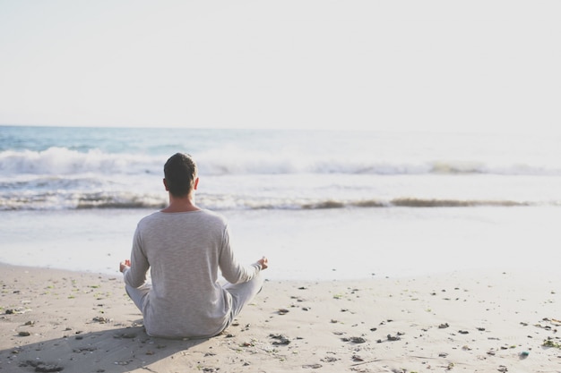 De yoga van de jonge mensenpraktijk op het strand bij zonsondergang.