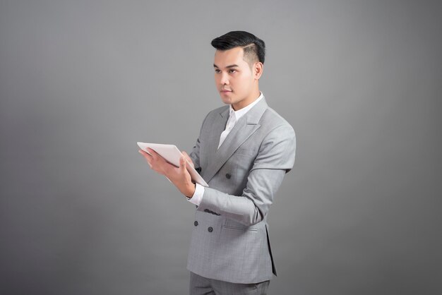 De zakenman gebruikt tablet, portret op studio grijze achtergrond