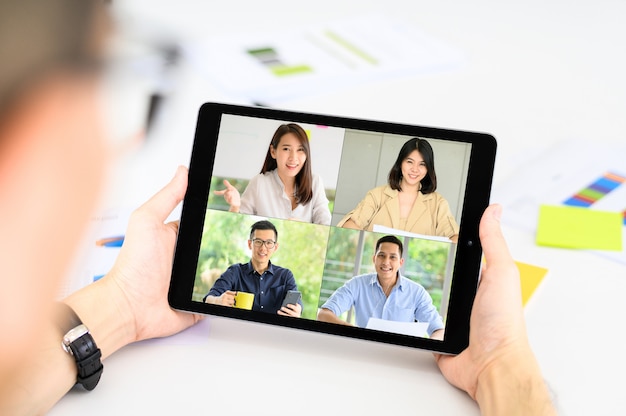 De zakenman heeft een vergadering met Asain-collega's over plan in videoconferentie via tablet