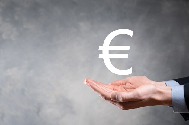 De zakenman houdt de pictogrammen van het geldmuntstuk EUR of Euro op donkere toonachtergrond. Het kweken van geldconcept voor bedrijfsinvesteringen en financiën.