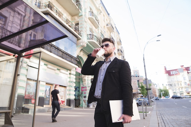 De zakenman met laptop in zijn handen bevindt zich op de achtergrond van stadsarchitectuur