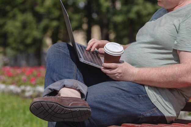 De zakenman zit bij het park en gebruikt laptop. Zakenman die openlucht laptop met behulp van