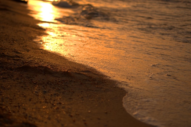 De zandige kust van de Zee van Azov bij zonsondergang een warme zomeravond de golven slaan tegen de kust strelen het zand met zeeschuim defocus selectieve focus