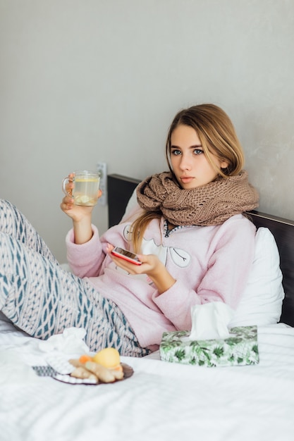 De zieke ongelukkige jonge vrouw ligt in een bed met hete thee