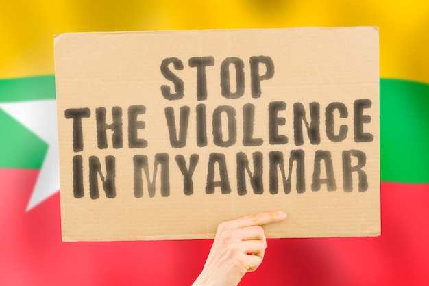 De zin Stop het geweld in Myanmar staat op een spandoek in mannenhanden met een wazige Myanmarese vlag op de achtergrond Trieste rechten Veiligheid Sociale stress Bestrijding van haat Wreedheid