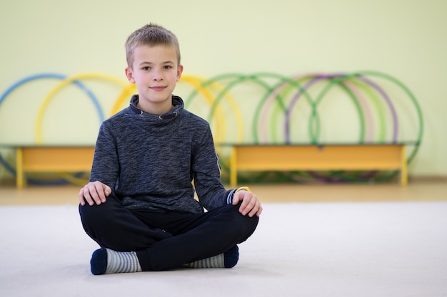 De zitting en de relaxiong van de jong kindjongen op de vloer binnen sportenruimte in een school na opleiding.