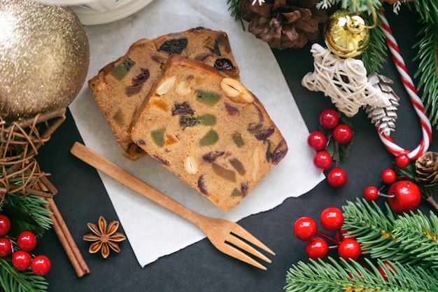 De zoete plakjes van de fruitcake op Witboek gezet op zwarte granietlijst in hoogste meningsvlakte leggen met Kerstmisdecoratie