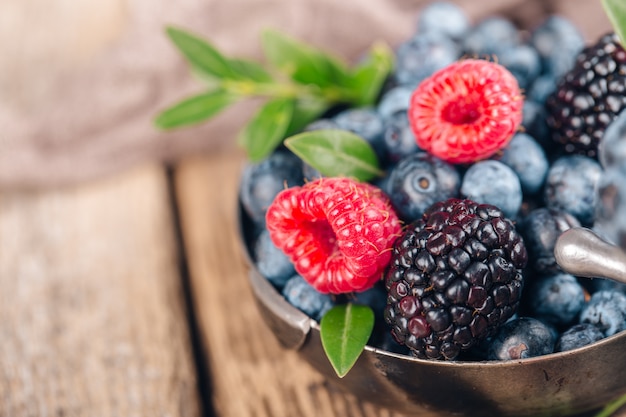 De zomerbessen mengen zich met Framboos, Bosbes en Blackberry in metaalschotels op houten achtergrond.