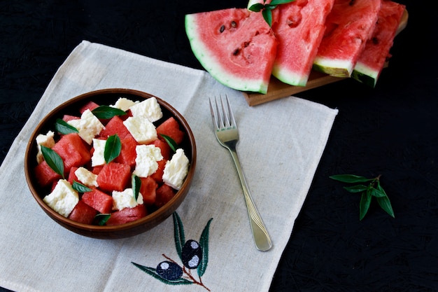 De zomersalade met watermeloen, witte kaas en basilicum in een kleiplaat op een zwarte achtergrond