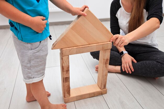 De zoon en moeder spelen in de kamer en bouwen het huis van houten blokken