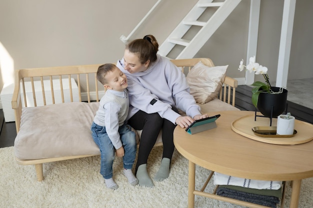 Foto de zoon omhelst zijn moeder en kijkt toe hoe haar moeder op een tablet werkt.