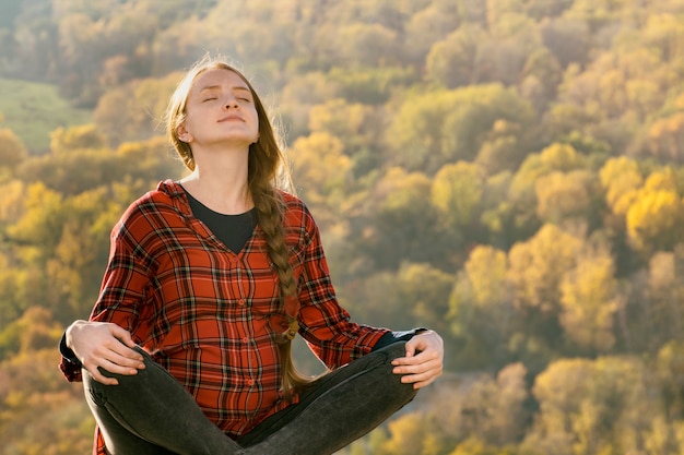 De zwangere vrouw zit op een heuvel met haar ogen dicht. meditatie. herfst bos