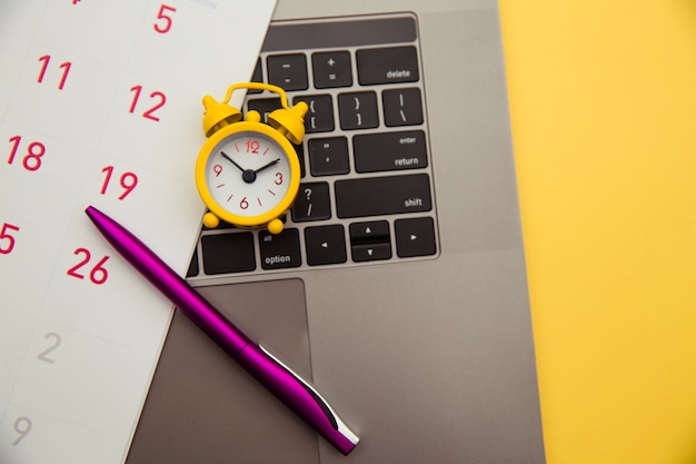 Foto concetto di scadenza. laptop e sveglia gialla, calendario mensile su sfondo giallo. il tempo sta scappando.