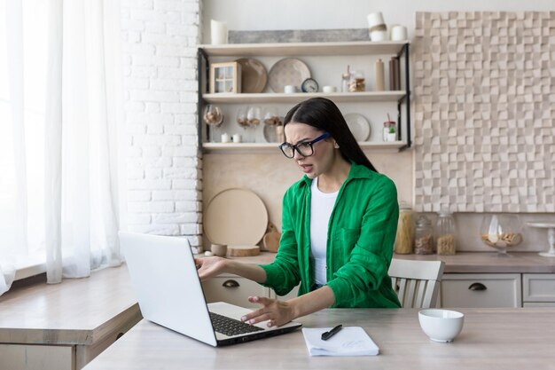 Deadline een mooie jonge zakenvrouw in glazen zit aan de tafel in de keuken werkt met een