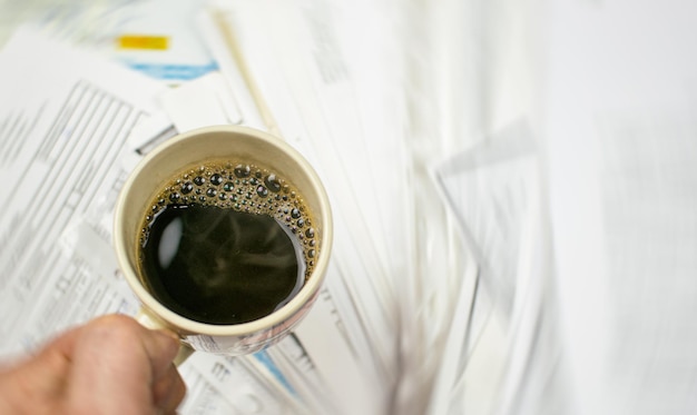 Deadline geschreven op papier en een kopje koffie in de hand tegen een achtergrond van verspreide papieren