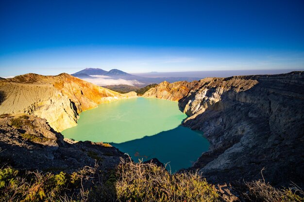 Foto albero senza foglie di legno morto con lago d'acqua turchesebella natura paesaggio montagna e lago verde al vulcano kawah ijen java orientale indonesia