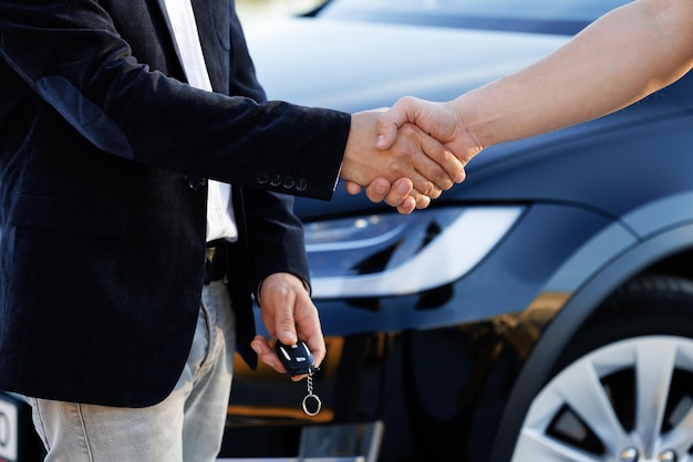 Foto il rivenditore che dà la chiave al nuovo proprietario in un salone di auto o in un salone la mano maschile dà le chiavi di un'auto alla mano maschile