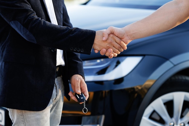 Фото Дилер дает ключ новому владельцу в автосалоне или салоне мужская рука дает ключи от машины мужской руке