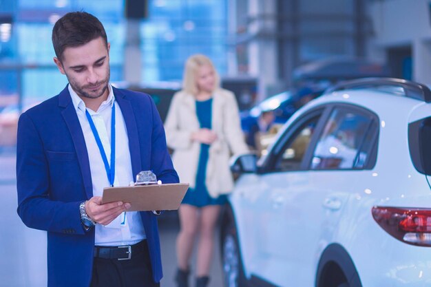 Dealer met vrouw staat bij een nieuwe auto in de showroom