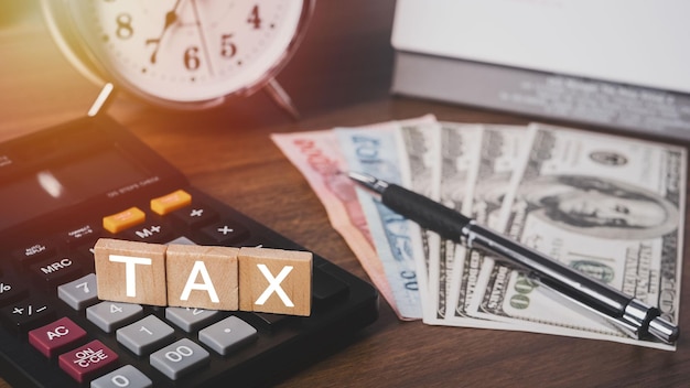 Photo debt collection and tax season concept. the word tax written in wooden block letters with calculator, money, clock, pen, background, time to pay concept