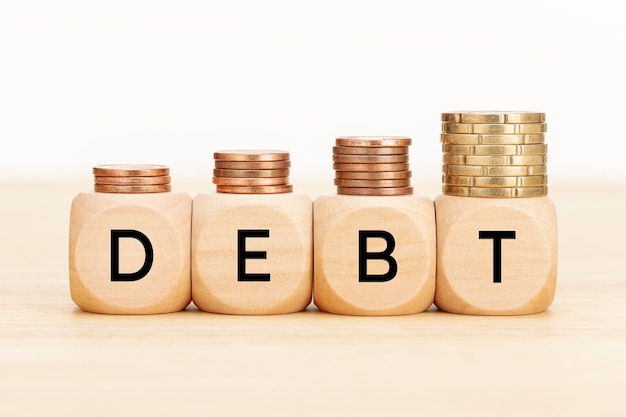 Debt concept. Wooden blocks with text and coins on wooden table. Copy space 