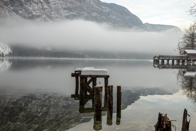 Decaying wooden pier in winter lake Bohinj with mountains in background and myst above the water