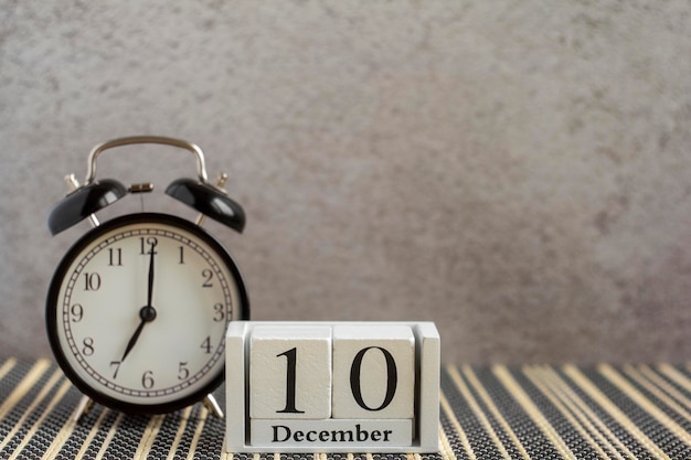 10 декабря на деревянном календаре рядом с будильником на темном столе. Один день зимы. Привет, декабрь, Привет, зима.