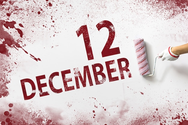 写真 12月12日。月の12日目、カレンダーの日付。手は赤いペンキでローラーを保持し、白い背景にカレンダーの日付を書き込みます。冬の月、年の日の概念。