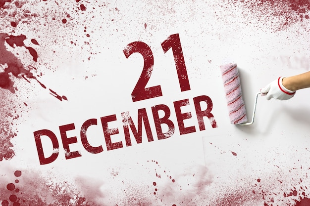 December 21st . Day 21 of month, Calendar date. The hand holds a roller with red paint and writes a calendar date on a white background. Winter month, day of the year concept.