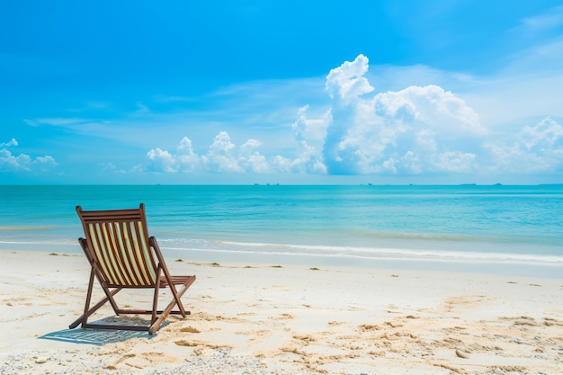 a deck chair on the beach with a blue sky and clouds