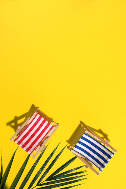 Deck chair with hard shadow palm leaves on yellow paper background flat lay and copy space summer travel vacation concept minimal composition