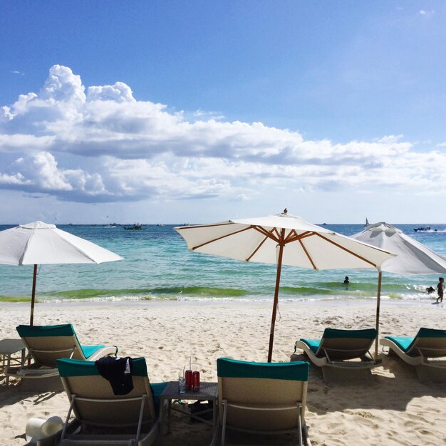 Deck chairs on beach against sky