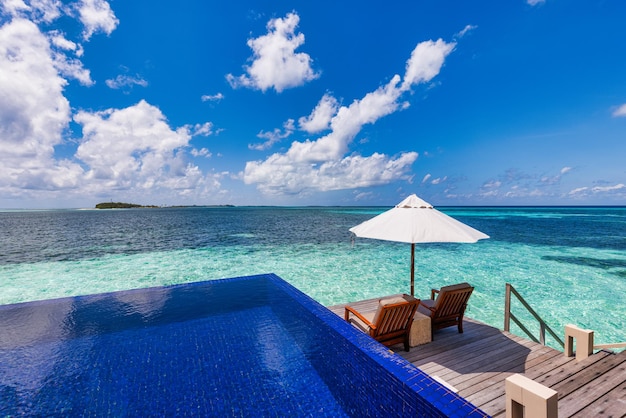 Deck chairs umbrellas at Maldives resort with infinity pool and beach, sea sky view. Luxury terrace