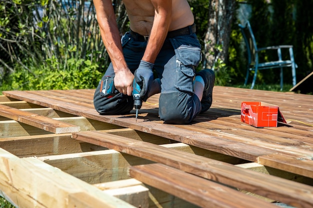 Deck construction builder hand with electric screwdriver installing impregnated wooden boards