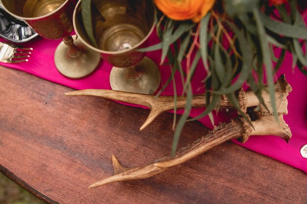 Decor. Details. Bridal bouquet. Composition. Wedding decorations. On the wooden table in the woods there is a flower arrangement with red, yellow, pink flowers and greenery, candles, statuettes.