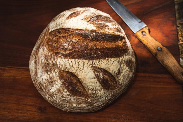 Decorated artisan made round loaf bread on wooden cutting board with knife