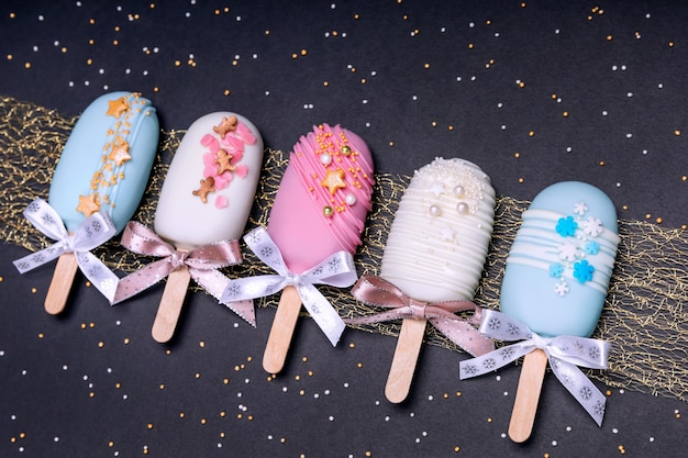 Decorated cake pops ice creams with bows on black background. Top view.